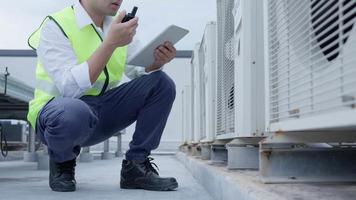 l'ingénieur utilise le walky talky pour expliquer les travaux sur le toit de l'usine. l'entrepreneur inspecte le système de compresseur et planifie l'installation de systèmes de climatisation sur le chantier de construction de bâtiments modernes. video