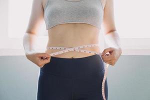 hermosa mujer gorda con cinta métrica usa su mano para exprimir el exceso de grasa que está aislado en un fondo blanco. ella quiere perder peso, el concepto de cirugía y descomponer grasa bajo el foto