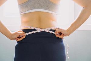 hermosa mujer gorda con cinta métrica usa su mano para exprimir el exceso de grasa que está aislado en un fondo blanco. ella quiere perder peso, el concepto de cirugía y descomponer grasa bajo el foto