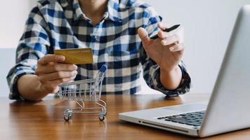 manos sosteniendo la tarjeta de crédito y usando la computadora portátil. las compras en línea foto