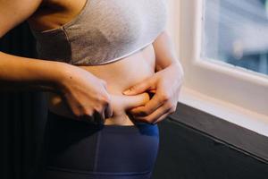 hermosa mujer gorda con cinta métrica usa su mano para exprimir el exceso de grasa que está aislado en un fondo blanco. ella quiere perder peso, el concepto de cirugía y descomponer grasa bajo el foto