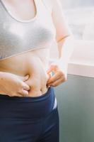 hermosa mujer gorda con cinta métrica usa su mano para exprimir el exceso de grasa que está aislado en un fondo blanco. ella quiere perder peso, el concepto de cirugía y descomponer grasa bajo el foto