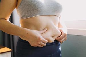 hermosa mujer gorda con cinta métrica usa su mano para exprimir el exceso de grasa que está aislado en un fondo blanco. ella quiere perder peso, el concepto de cirugía y descomponer grasa bajo el foto