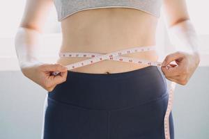 hermosa mujer gorda con cinta métrica usa su mano para exprimir el exceso de grasa que está aislado en un fondo blanco. ella quiere perder peso, el concepto de cirugía y descomponer grasa bajo el foto