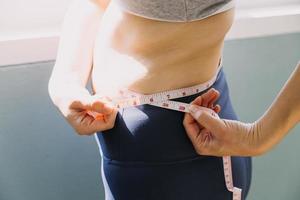 hermosa mujer gorda con cinta métrica usa su mano para exprimir el exceso de grasa que está aislado en un fondo blanco. ella quiere perder peso, el concepto de cirugía y descomponer grasa bajo el foto