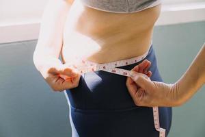 hermosa mujer gorda con cinta métrica usa su mano para exprimir el exceso de grasa que está aislado en un fondo blanco. ella quiere perder peso, el concepto de cirugía y descomponer grasa bajo el foto