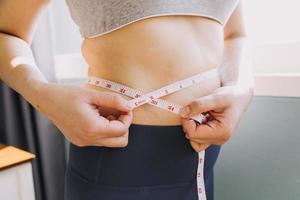 hermosa mujer gorda con cinta métrica usa su mano para exprimir el exceso de grasa que está aislado en un fondo blanco. ella quiere perder peso, el concepto de cirugía y descomponer grasa bajo el foto