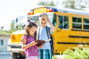 riendo sonriente niño caucásico estudiante niño con expresión de cara divertida caminando cerca del autobús amarillo el 1 de septiembre. educación y concepto de regreso a la escuela. niño alumno listo para aprender y estudiar. foto