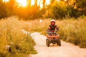 The little girl rides a quad bike ATV. A mini quad bike is a cool girl in a helmet and protective clothing. Electric quad bike electric car for children popularizes green technology. photo