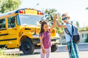 beautiful little schoolgirl with classmates near school bus photo