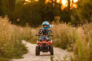 A little boy wearing a helmet riding a quad bike on the shore of a mountain river. photo
