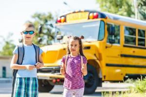 beautiful little schoolgirl with classmates near school bus photo