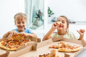 Two little girls eating pizza at home photo