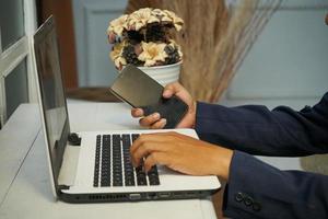 hombre de negocios asiático manos trabajando en la oficina con computadora portátil y teléfono móvil, escribiendo en el teclado en su escritorio, cerrar foto