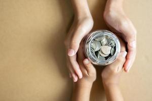 Kid hands holding coins in a jar together as saving concept for family or education. photo
