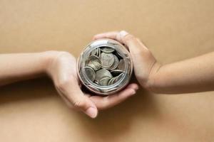 Kid hands holding coins in a jar together as saving concept for family or education. photo