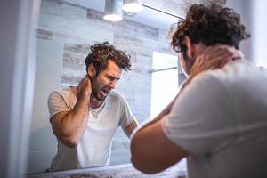 Portrait of sleepy young man yawning and looking at mirror in bathroom in morning, side view. Trying to wake up. Lack of sleep, insomnia and stressful lifestyle. Hangover. depression. photo