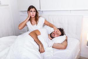 Couple in bed, man snoring and woman can't sleep. Snoring man and young woman. Couple sleeping in bed. Young girl can't sleep because of her man's snoring holding his nose. Snoring man problem photo