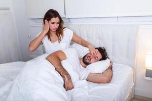 Couple in bed, man snoring and woman can't sleep. Snoring man and young woman. Couple sleeping in bed. Young girl can't sleep because of her man's snoring holding his nose. Snoring man problem photo