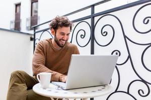 Businessman working on computer, drinking coffee and smiling, business man entrepreneur working on computer, businessman reading emails and holding his mobile phone photo