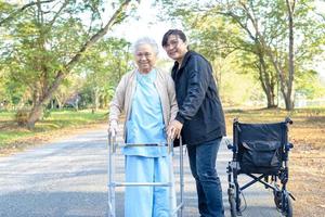 cavernícola ayuda y cuida a una anciana asiática o anciana con buena salud mientras camina en el parque en felices vacaciones frescas. foto