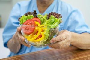 Asian senior or elderly old lady woman patient eating breakfast vegetable healthy food with hope and happy while sitting and hungry on bed in hospital. photo