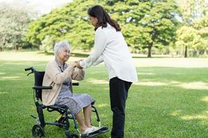 cuidador ayuda y cuida a una anciana asiática o anciana paciente sentada en silla de ruedas en el parque, concepto médico fuerte y saludable. foto