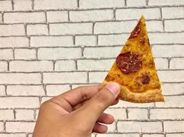 hand held pizza slice against white brick wall background photo