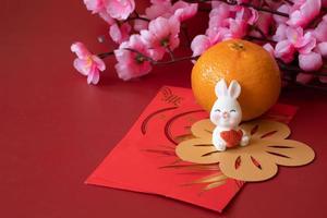 Chinese New Year of the rabbit festival concept. Mandarin orange, red envelopes, rabbit and gold ingot decorated with plum blossom on red background. photo