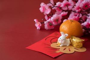 Chinese New Year of the rabbit festival concept. Mandarin orange, red envelopes, rabbit and gold ingot decorated with plum blossom on red background. photo