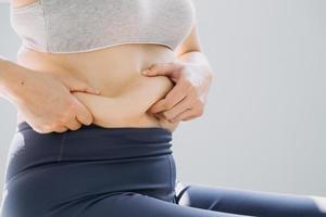 hermosa mujer gorda con cinta métrica usa su mano para exprimir el exceso de grasa que está aislado en un fondo blanco. ella quiere perder peso, el concepto de cirugía y descomponer grasa bajo el foto