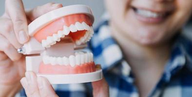 concepto de estomatología, retrato parcial de una chica con fuertes dientes blancos mirando la cámara y sonriendo, con los dedos cerca de la cara. primer plano, de, mujer joven, en, dentista, estudio, adentro foto