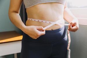 hermosa mujer gorda con cinta métrica usa su mano para exprimir el exceso de grasa que está aislado en un fondo blanco. ella quiere perder peso, el concepto de cirugía y descomponer grasa bajo el foto