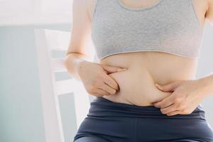 hermosa mujer gorda con cinta métrica usa su mano para exprimir el exceso de grasa que está aislado en un fondo blanco. ella quiere perder peso, el concepto de cirugía y descomponer grasa bajo el foto