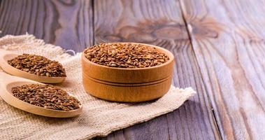 Brown flax seeds or flax seed in a small bowl on sacking and two wooden false on wooden table photo