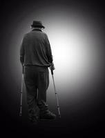 The smiling senior man with two crutches moving from the darkness into the circle of light photo