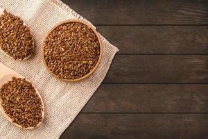 Brown flax seeds or flax seed in a small bowl on sacking and two wooden false on a brown wooden table photographed from above photo