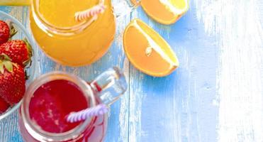 Orange and strawberry juice in glass on old wooden blue table photo