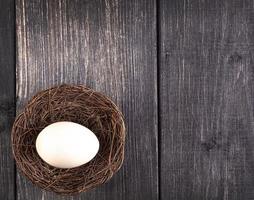 The white egg on the nest on the old wooden background photo