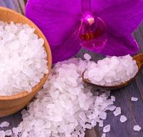 White bath salt in a wooden cup with a spoon on a wooden table with an orchid. photo