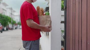 uno donna ordinato cibo in linea per mangiare a casa. il persona ordini prodotti o cibo in linea, riceve pacchi a partire dal consegna uomo quello mettere un' maschera su il porta di il Casa. video