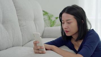 asiatico donna con depresso facciale espressione seduta uso Telefono per Seguire marito perché amore problema. triste femmina nel sua camera. amore problema concetto. video