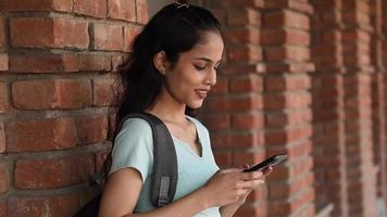 vídeo de estoque de uma adolescente indiana em um campus universitário digitando em seu telefone e exibindo a tela olhando para a câmera. video