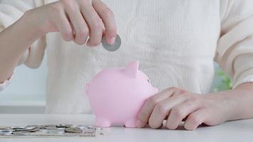 closeup woman hand putting money coin into piggy bank for saving money. wealth, Finance, business, investment, retirement, future, accounting, plan life, economize, conserve, family, health.