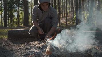 Young hiker male kindling a fire in the mountains. Traveler man lighting a fire in the camp near the tent while spending time in the nature. Travel and lifestyle concept. video