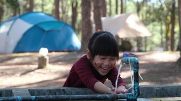 Cute Asian little girl washing her hands in the park. Little girl washing her hands under the faucet after doing a coloring activity near the tent. clean and Hygiene concept. video