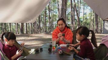 las madres y los niños felices pasan las vacaciones de invierno juntos en un bosque de pinos, coloreando piñas para decorar el árbol de navidad. actividades de manualidades navideñas para niños a partir de piñas. video