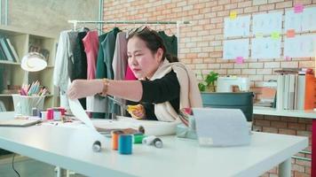 asiatisk medelålders kvinna mode designer Arbetar i studio, skärande och välja tyg mönster idéer med teckning skisser för klänning design samlingar. professionell boutique skräddare sme entreprenör. video