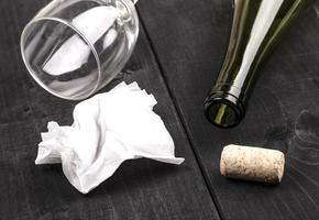 The used white crumpled paper napkin and an empty wine bottle with cork on old wooden table photo