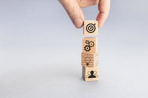 Business team strategy and action plan concept. Hand putting wood block with target icon on top of others with gear, light bulb and teamwork icons. Gray background. Copy space photo